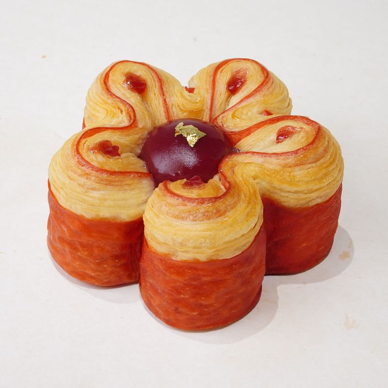 Lych'Y Pink · Bánh ngàn lớp hình bông hoa màu đỏ và kem, giữa có một viên tròn màu đỏ sẫm · Flower-shaped laminated pastry in red and cream with a dark red dome in the centre