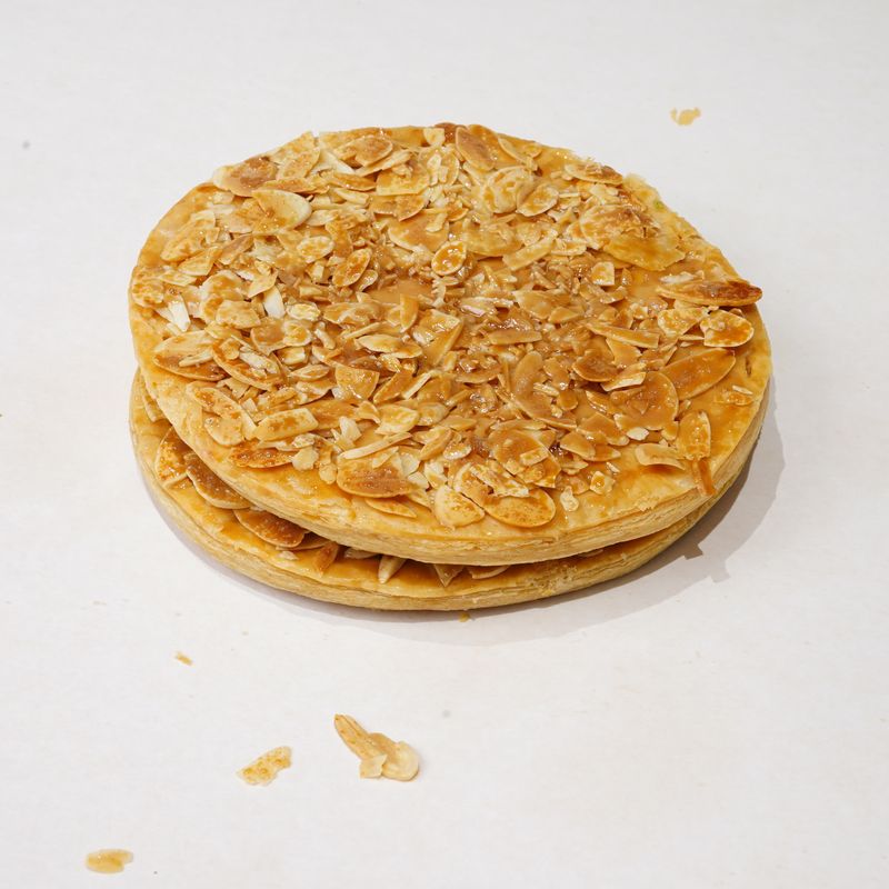 Florentine Cookie · Bánh tròn hai lớp phủ vụn giòn màu vàng nâu, vài mẩu vụn bên cạnh · Two-layer round pastry with a golden-brown crumb topping, a few crumbs beside it