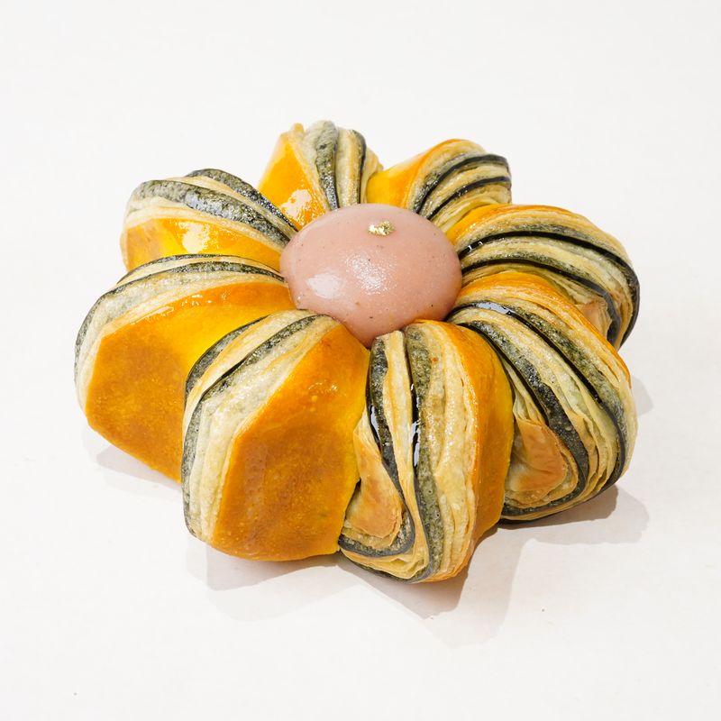 Pink Guava Twist · Bánh ngàn lớp hình bông hoa sọc cam và xanh sẫm, giữa có một viên kem màu hồng · Flower-shaped laminated pastry with orange and dark green stripes and a pink centre