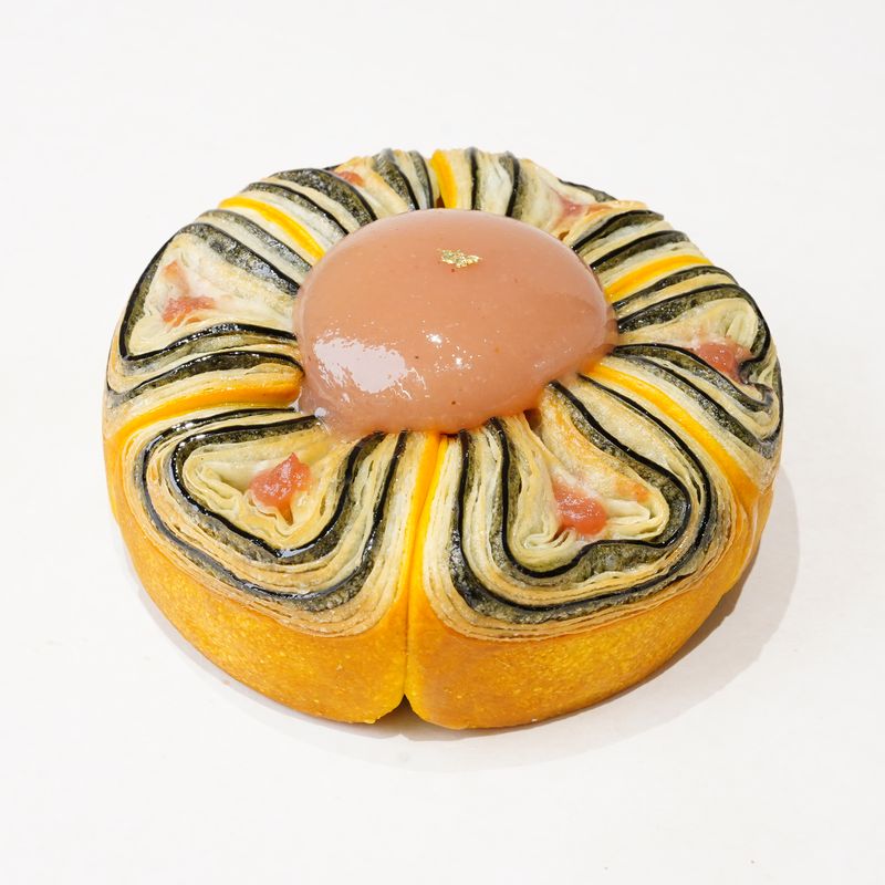 White Peach Jewel · Bánh ngàn lớp tròn với các vòng sọc vàng và xanh sẫm, giữa có lớp kem màu hồng nâu · Round laminated pastry with yellow and dark green swirled stripes and a pinkish-brown centre