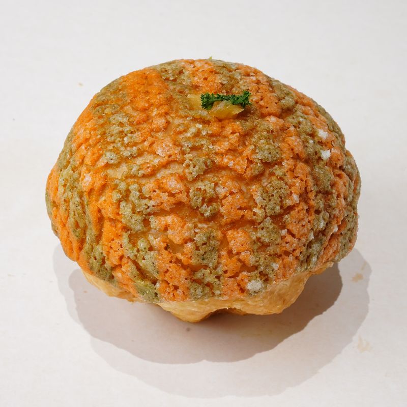 Melon Bloom · Bánh tròn với lớp vỏ giòn nứt màu cam và xanh, điểm trang trí xanh nhỏ ở trên · Round pastry with an orange and green crackled crust and a small green garnish